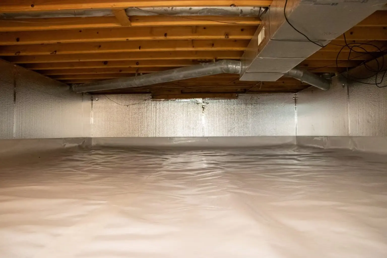 Clean crawl space lined with a full vapor barrier under wooden floor joists